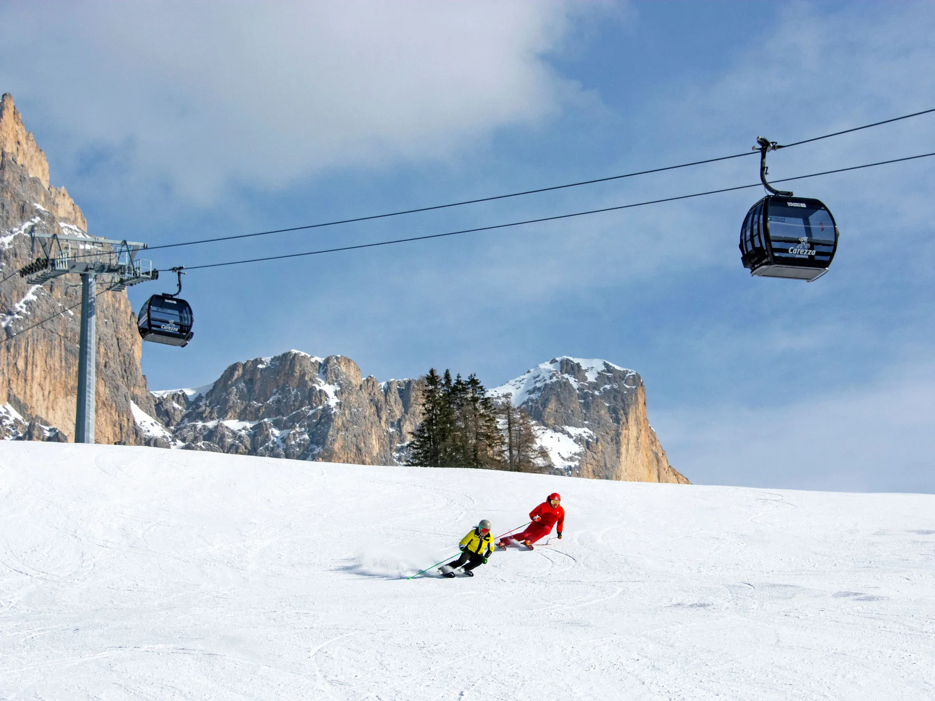 Ihr werdet dieses Skihotel in den Dolomiten lieben. Skilift und zwei Skifahrer auf verschneiter Piste vor Bergkulisse