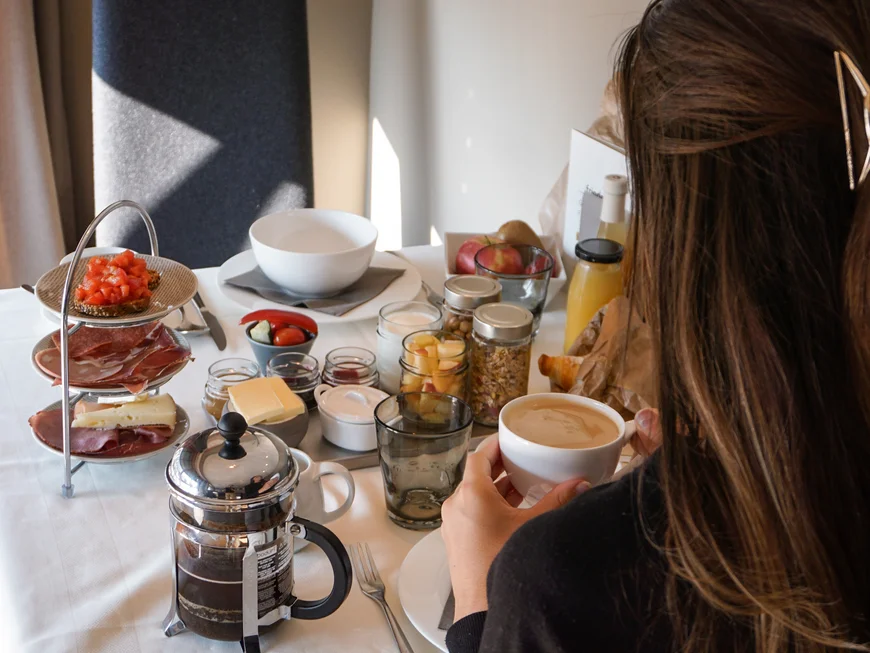 Auf ins Genusshotel nach Südtirol! Frau trinkt Kaffee am Tisch mit Frühstück und Küchenutensilien