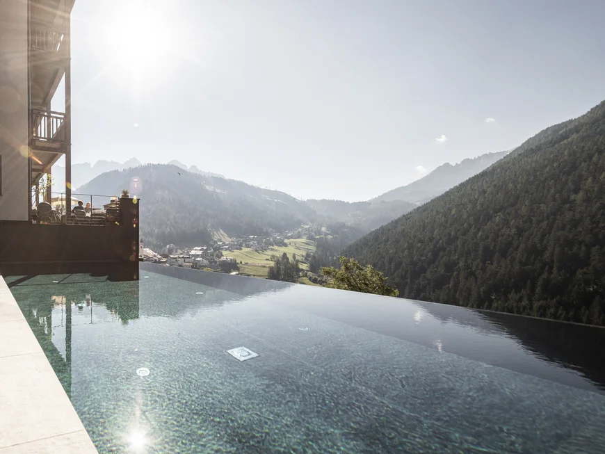 Euer Hotel mit Infinitypool in den Dolomiten Infinity-Pool mit Bergblick und Sonnenschein an einem klaren Tag