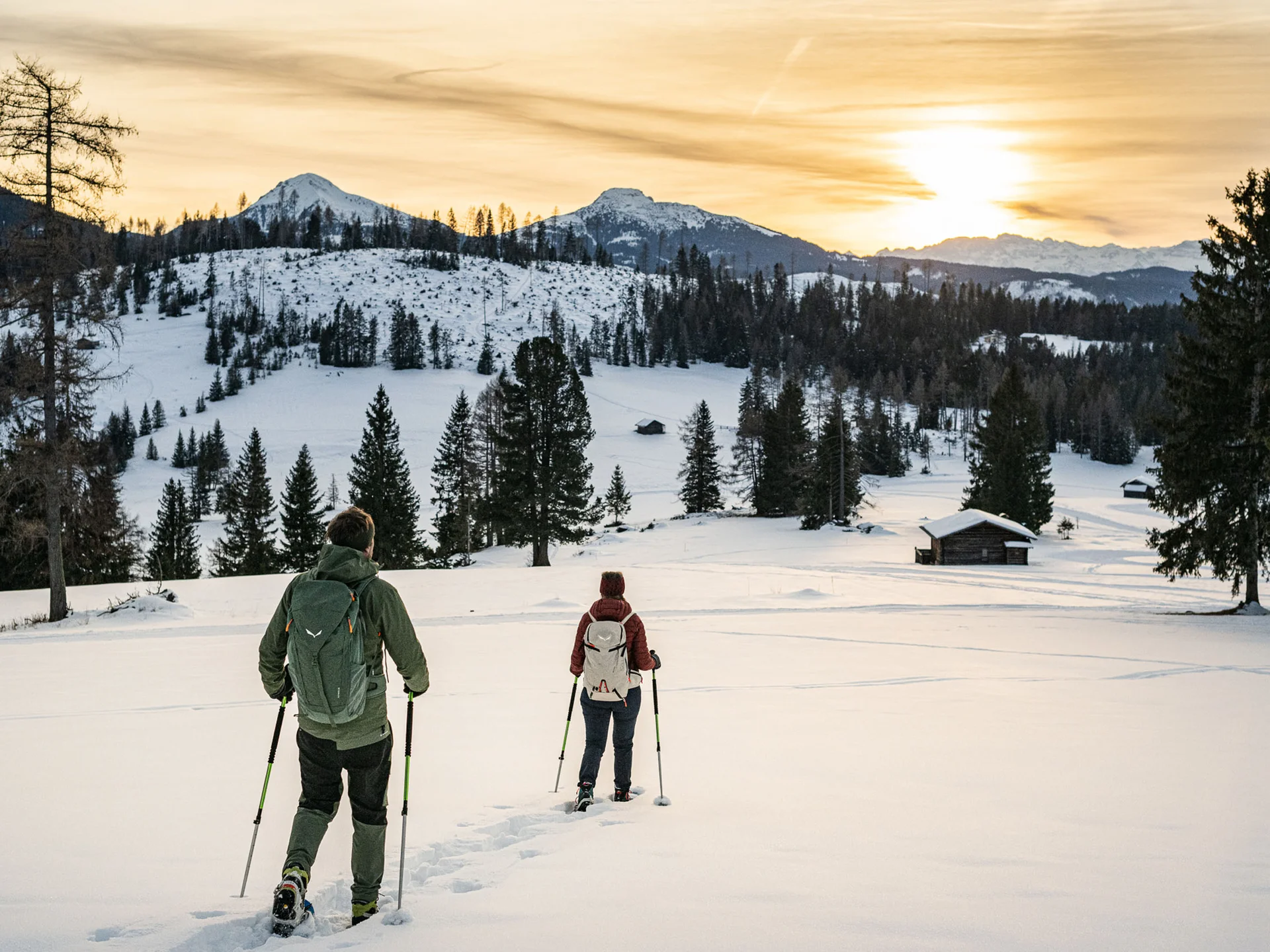 Ihr werdet dieses Skihotel in den Dolomiten lieben. Zwei Personen beim Schneeschuhwandern in verschneiter Berglandschaft bei Sonnenuntergang