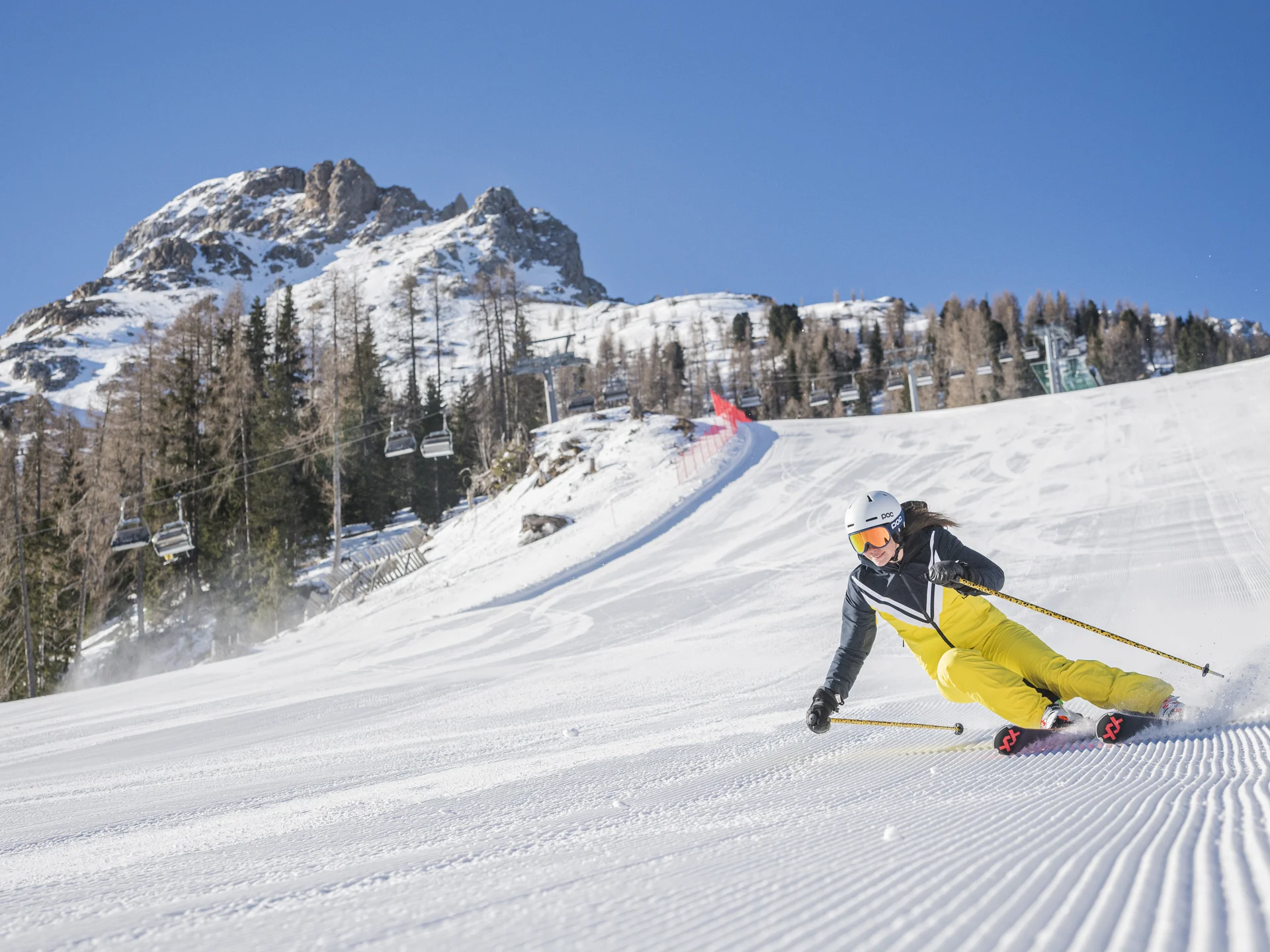 Ihr werdet dieses Skihotel in den Dolomiten lieben. Skifahrer in gelber Kleidung fährt auf präparierter Piste vor Bergkulisse