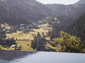Friedrich ist DAS Boutiquehotel in den Dolomiten Infinity-Pool mit Blick auf Tal und bewaldete Hügel bei klarem Himmel