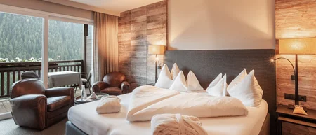 Gemütliches Hotelzimmer mit Bett, zwei Sesseln und Balkon mit Waldsicht