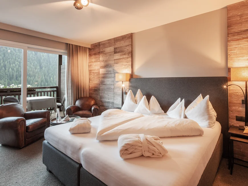 Das feinste Adults-only-Hotel in den Dolomiten Gemütliches Hotelzimmer mit Bett, zwei Sesseln und Balkon mit Waldsicht