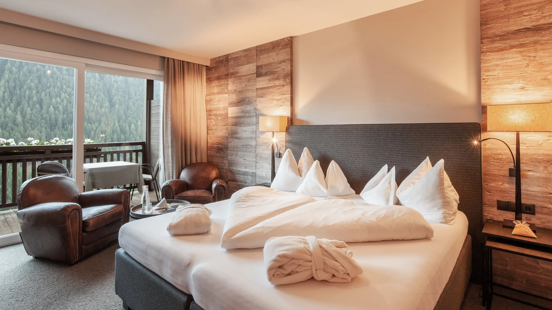 Gemütliches Hotelzimmer mit Bett, zwei Sesseln und Balkon mit Waldsicht