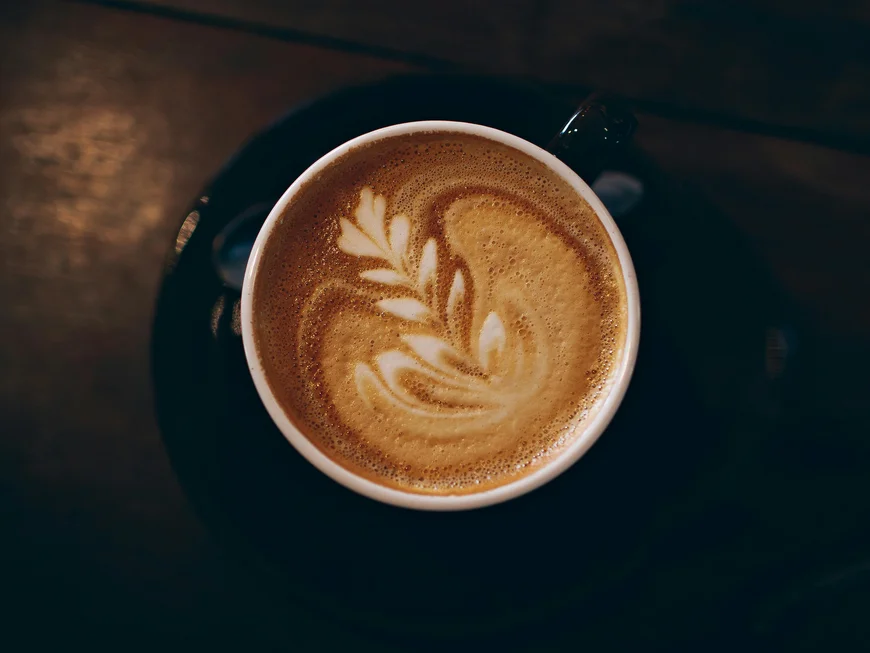 Regionale Küche in Südtirol Latte Macchiato mit Milchschaumkunst auf schwarzem Unterteller