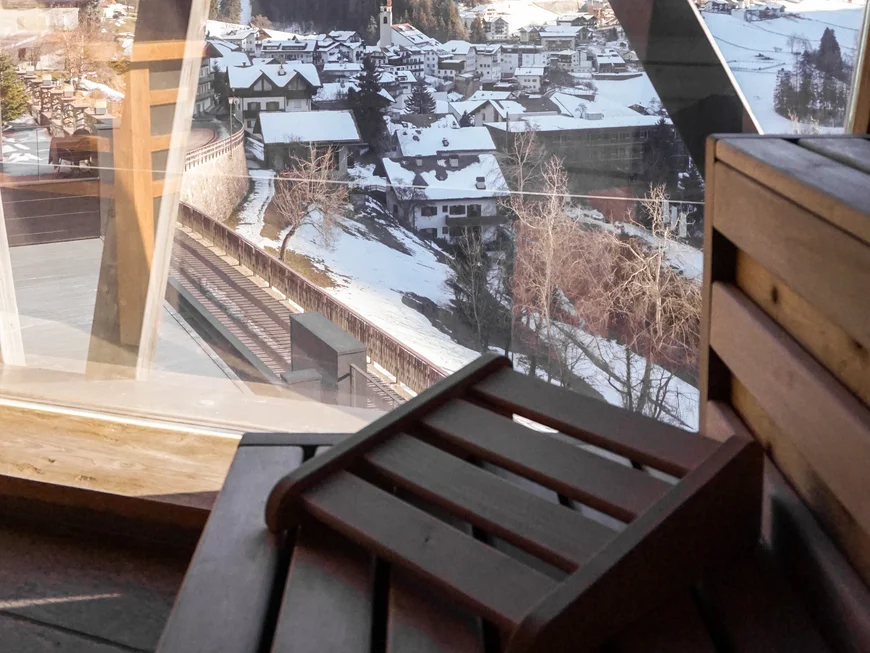 Ihr werdet dieses Skihotel in den Dolomiten lieben. Blick auf verschneites Dorf und Berge durch ein Fenster mit Holzrahmen