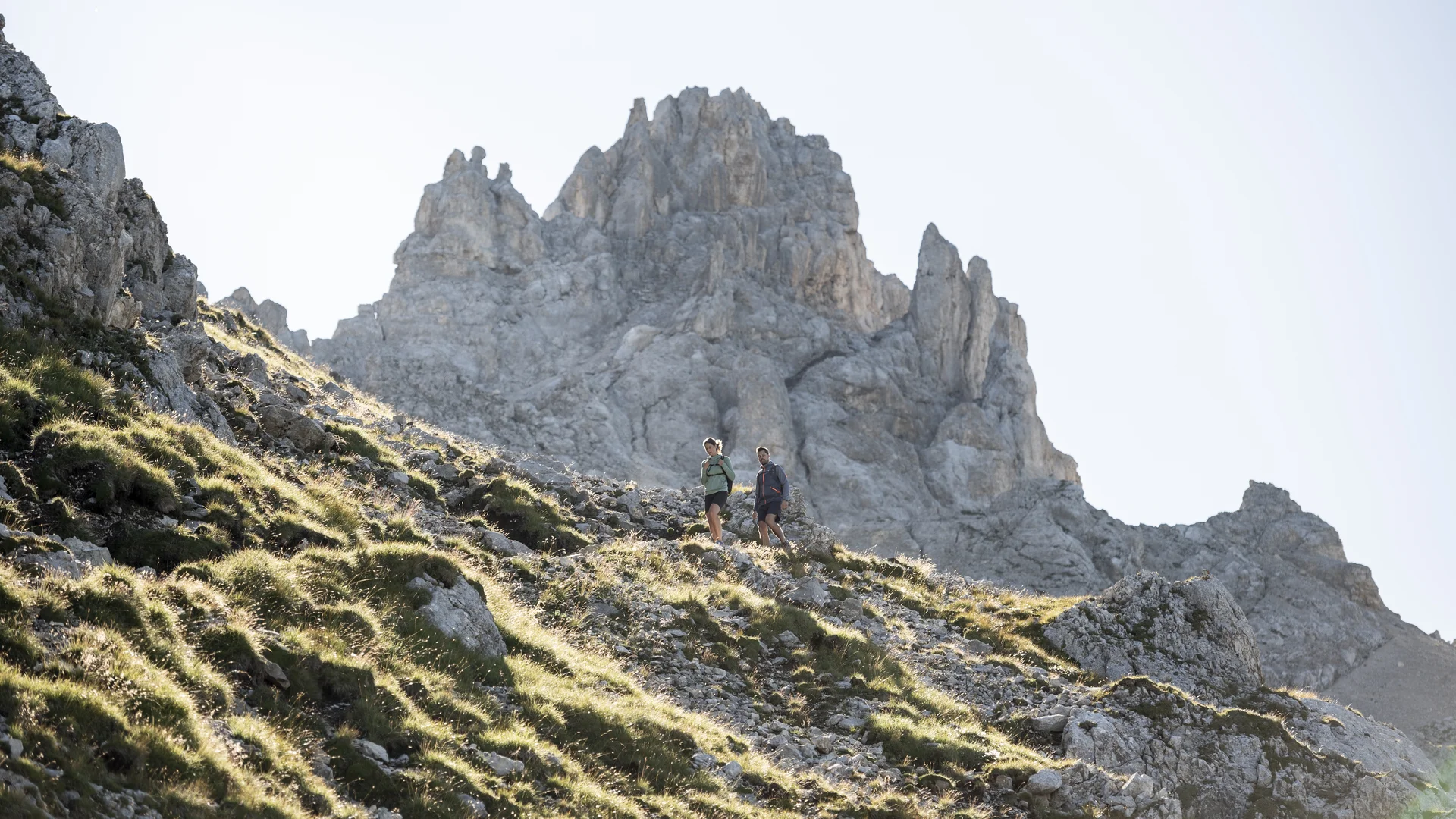 Zwei Wanderer auf bergigem Pfad vor steiniger Gipfelkulisse