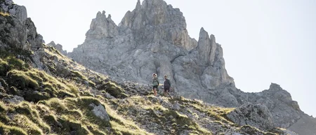 Zwei Wanderer auf bergigem Pfad vor steiniger Gipfelkulisse