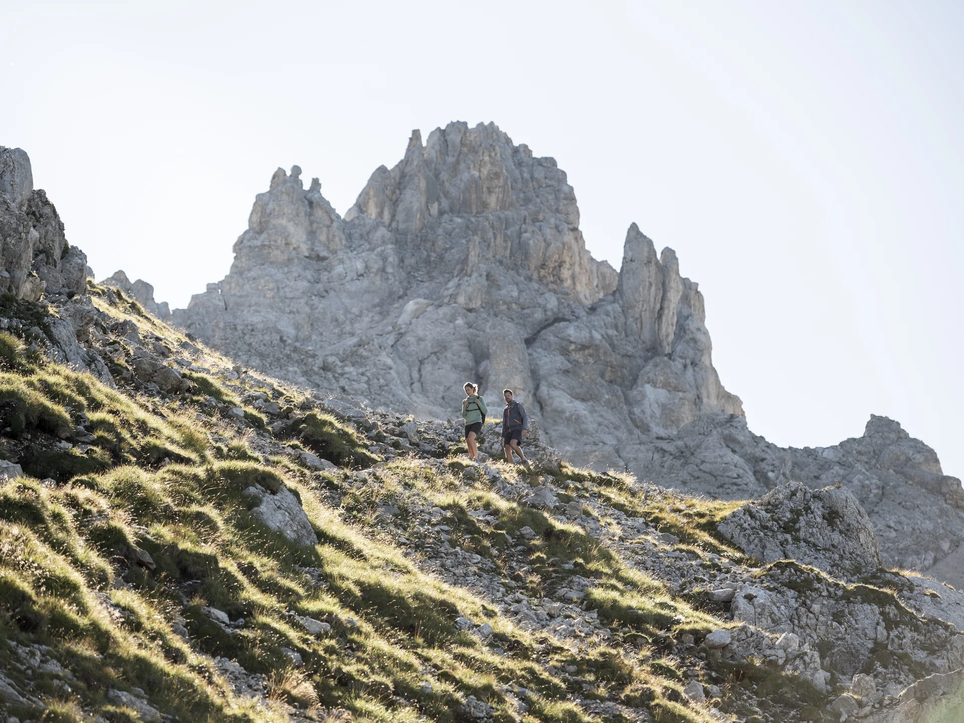 Seid ihr bereit für euren Sommerurlaub in den Dolomiten? Zwei Wanderer auf bergigem Pfad vor steiniger Gipfelkulisse