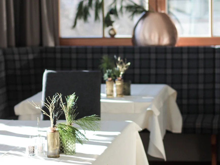 Auf ins Genusshotel nach Südtirol! Moderner Essbereich mit weißen Tischen und Grünpflanzen vor Fenster