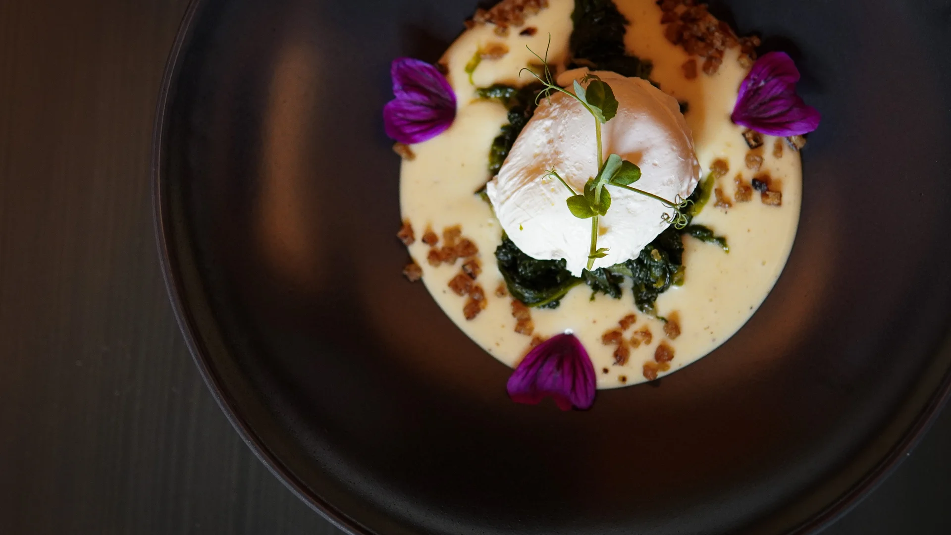 Friedrich ist DAS Boutiquehotel in den Dolomiten Pochiertes Ei auf Spinat mit cremiger Sauce und essbaren Blüten auf schwarzem Teller