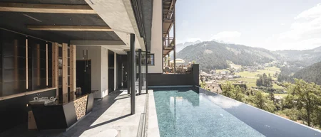 Infinity-Pool mit Bergblick an modernem Hotel in sonniger Landschaft