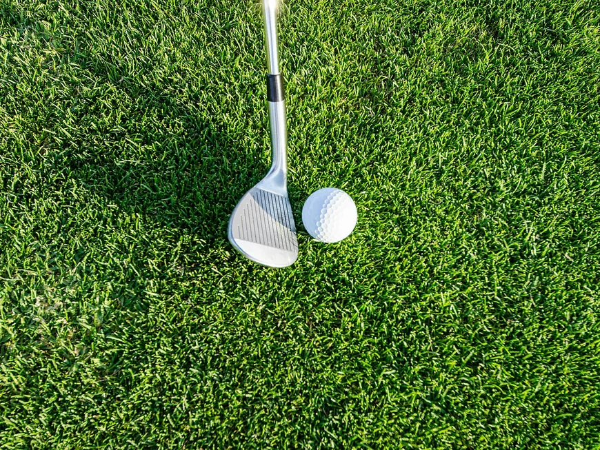 Golfball und Golfschläger auf grünem Rasen