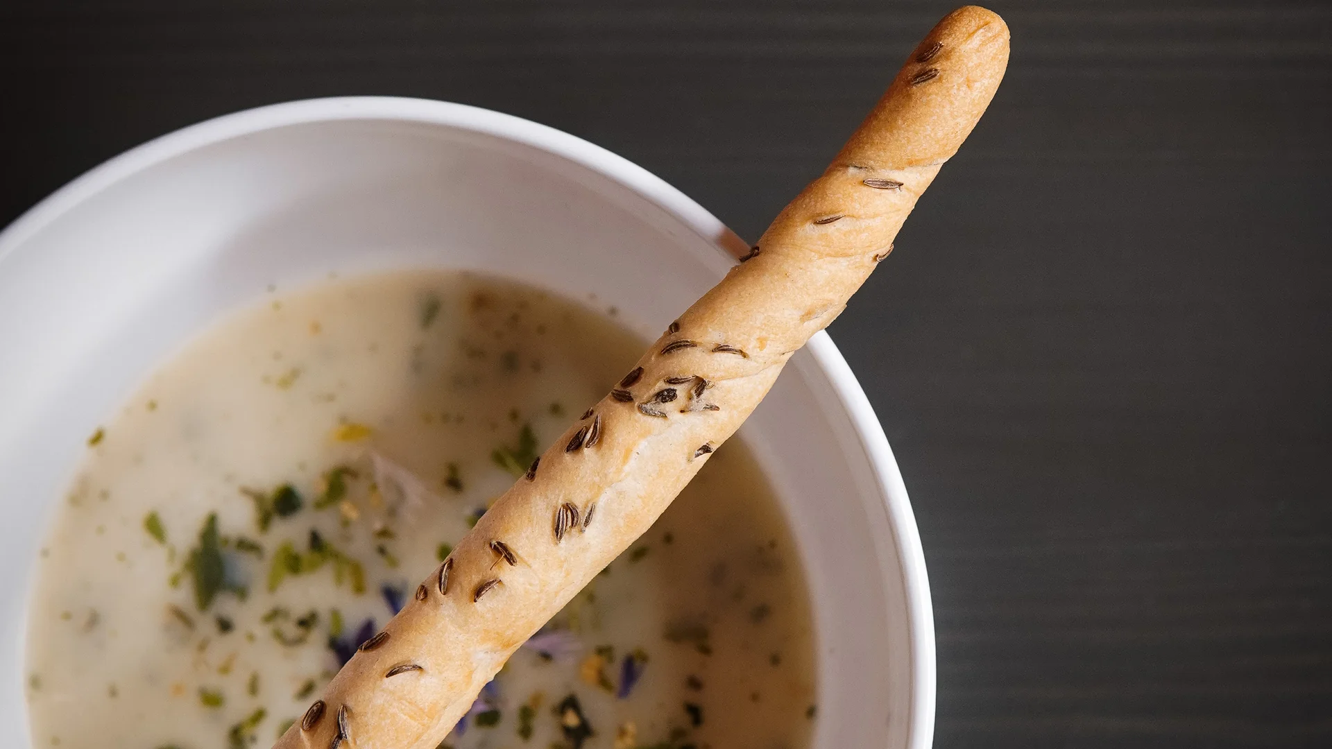 Weiße Schüssel mit cremiger Kräutersuppe und Brotstange mit Kümmel