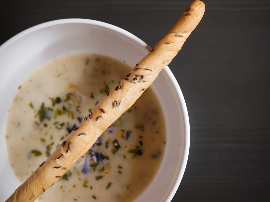 Es geht um das Abendessen. Weiße Schüssel mit cremiger Kräutersuppe und Brotstange mit Kümmel