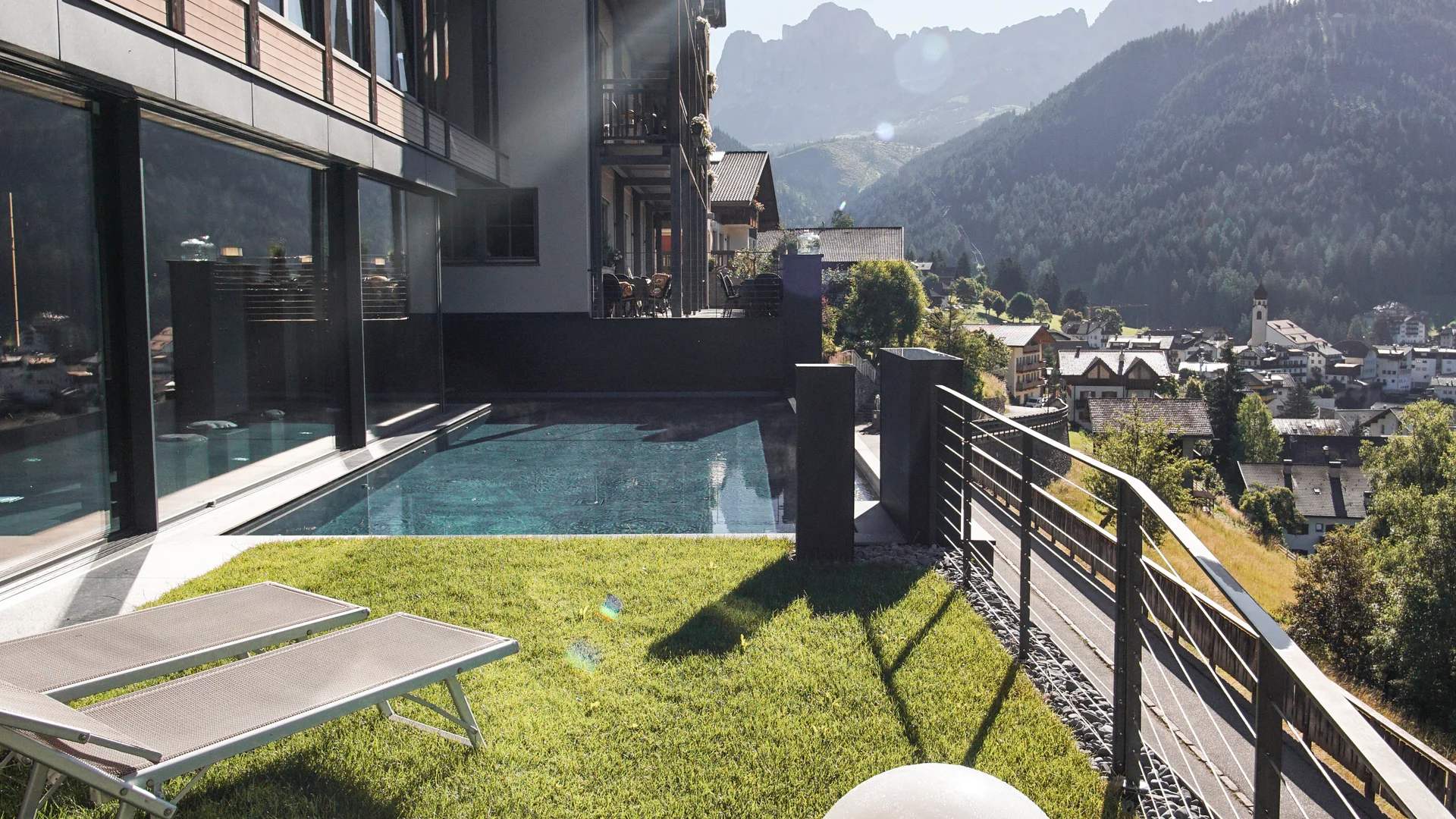 Hotel mit Pool, Liegestühlen und Bergblick bei Sonnenschein