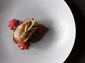Friedrich ist DAS Boutiquehotel in den Dolomiten Elegantes Gericht mit Fleisch, Sauce und Rosmarinzweigen auf weißem Teller