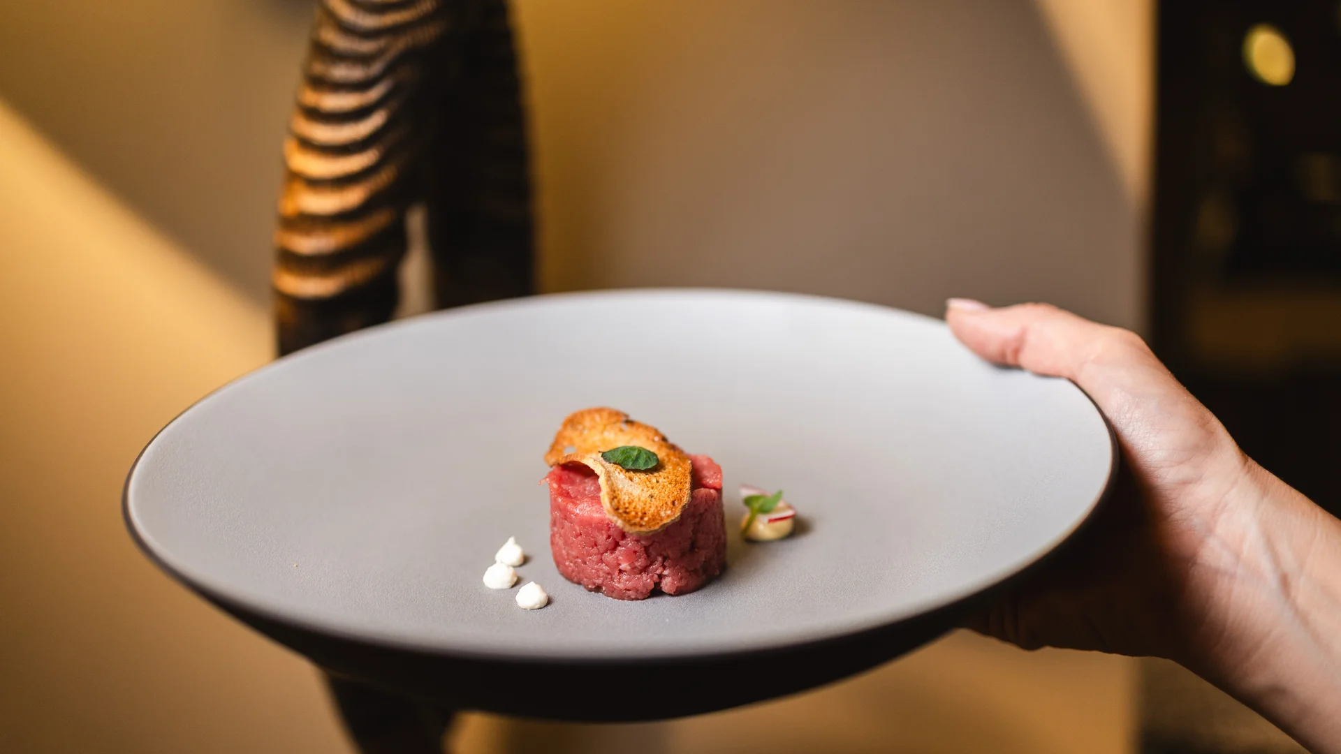 Hände halten Teller mit serviertem rohem Fleisch und Crostini