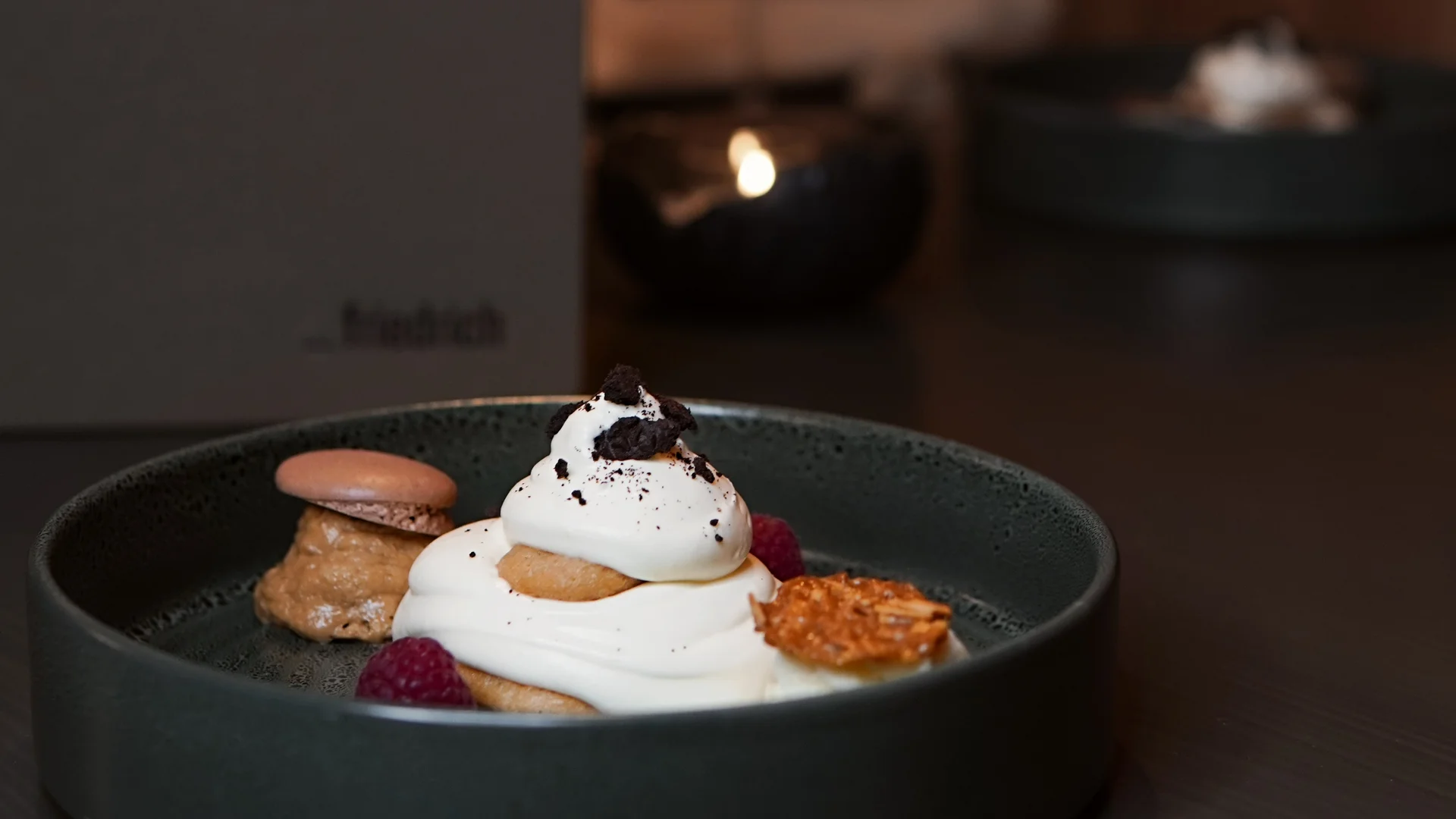 Dessert mit Sahne, Keks, Himbeeren und Karamell auf dunklem Teller