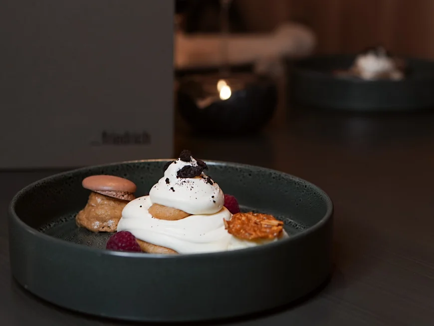 Es geht um das Abendessen. Dessert mit Sahne, Keks, Himbeeren und Karamell auf dunklem Teller