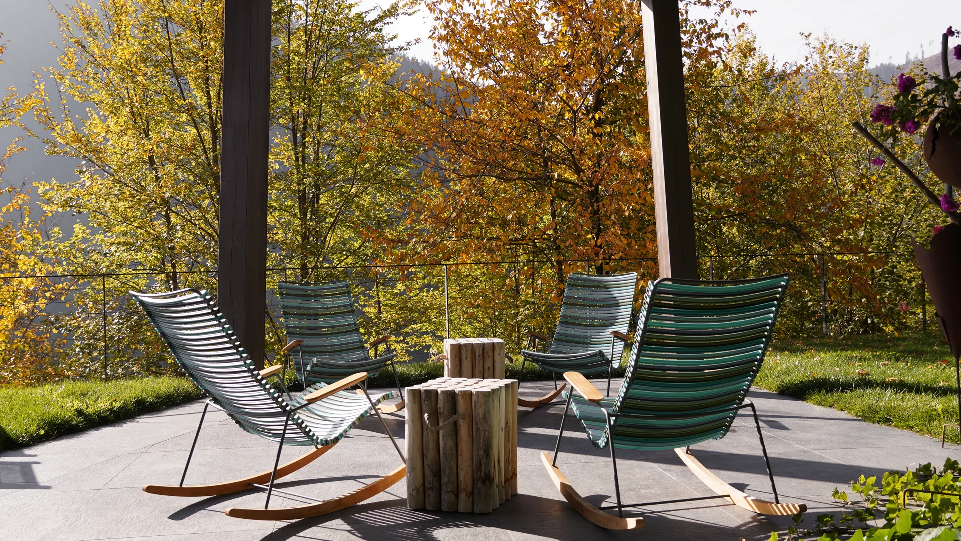 Vier moderne Schaukelstühle und ein Holztisch auf der Veranda mit Herbstbäumen