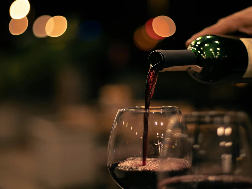 Wein und Bar | Friedrich Welschnofen Rotwein wird in ein Glas bei gedimmtem Licht eingeschenkt