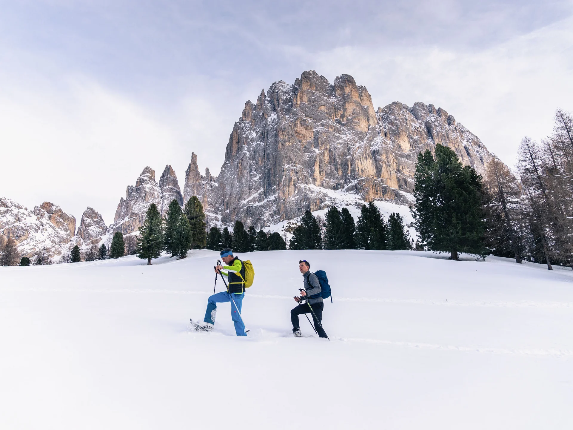 Ihr werdet dieses Skihotel in den Dolomiten lieben. Zwei Männer beim Schneeschuhwandern vor schneebedeckten Bergen und Bäumen