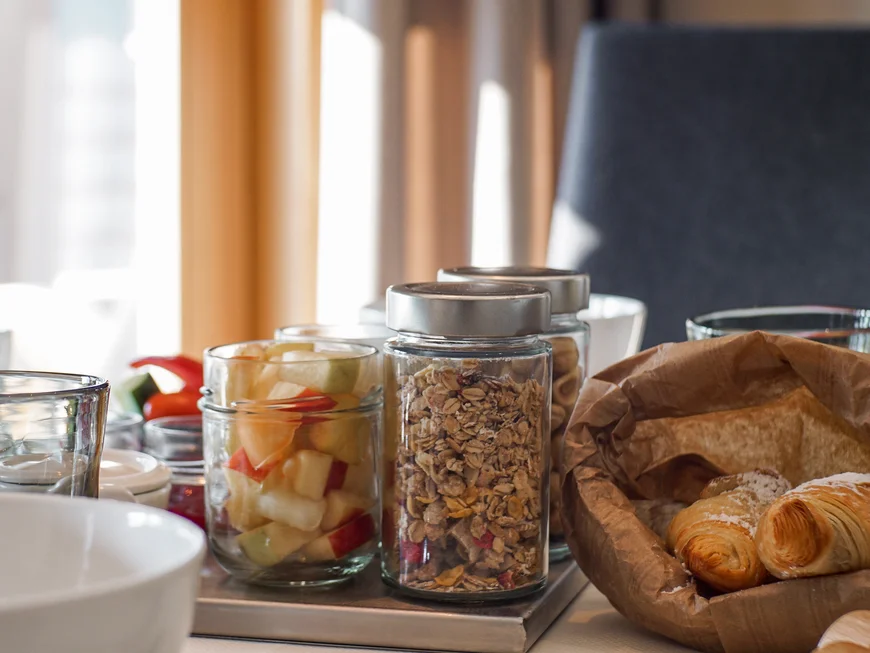 Das Friedrich Frühstück in Südtirol Frühstückstisch mit Müsli, Obstsalat und Croissants in Gläsern und Korb