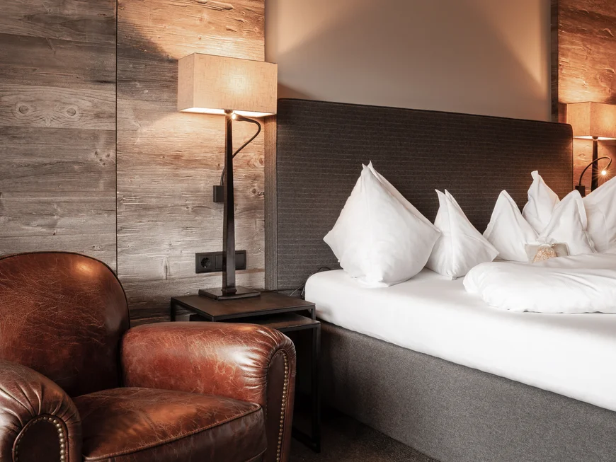 Das ist nicht irgendein nachhaltiges Hotel in Südtirol Gemütliches Hotelzimmer mit Ledersessel, Nachttischlampen und weißem Bett