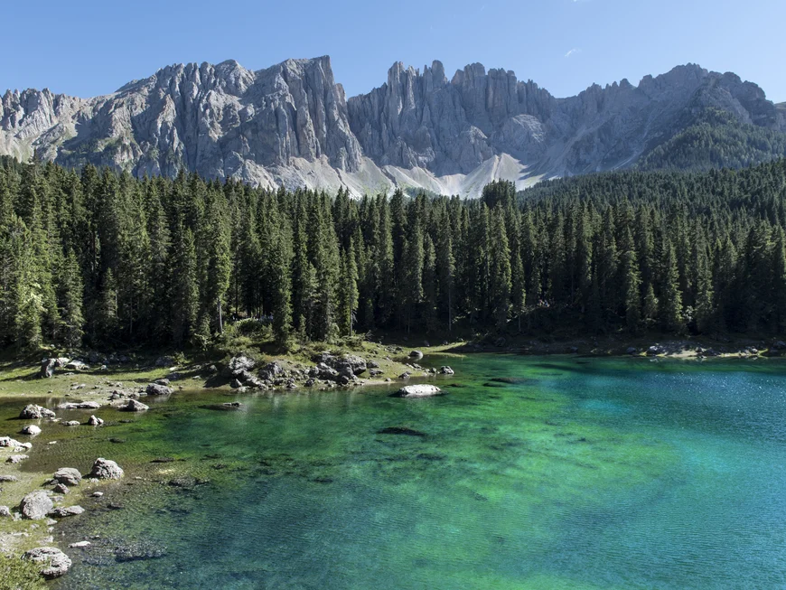 Das Aktivhotel in den Dolomiten für Erwachsene ab 14 Klarer Bergsee mit Tannenwald und spitzen Felsen unter blauem Himmel
