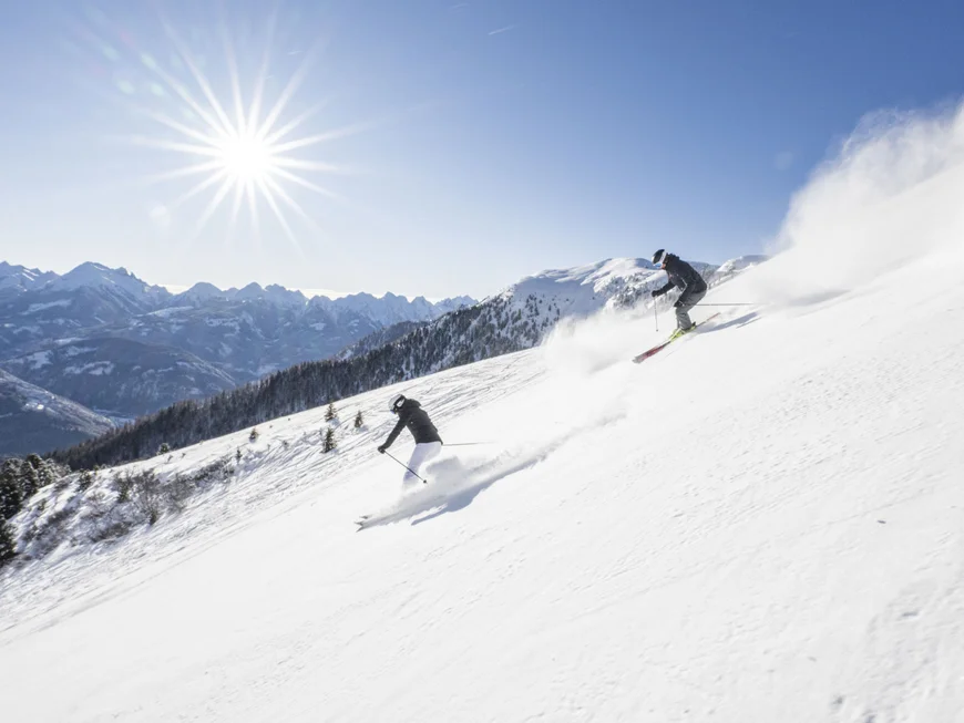 Ihr werdet dieses Skihotel in den Dolomiten lieben. Zwei Skifahrer fahren an sonnigem Tag einen verschneiten Berg ab