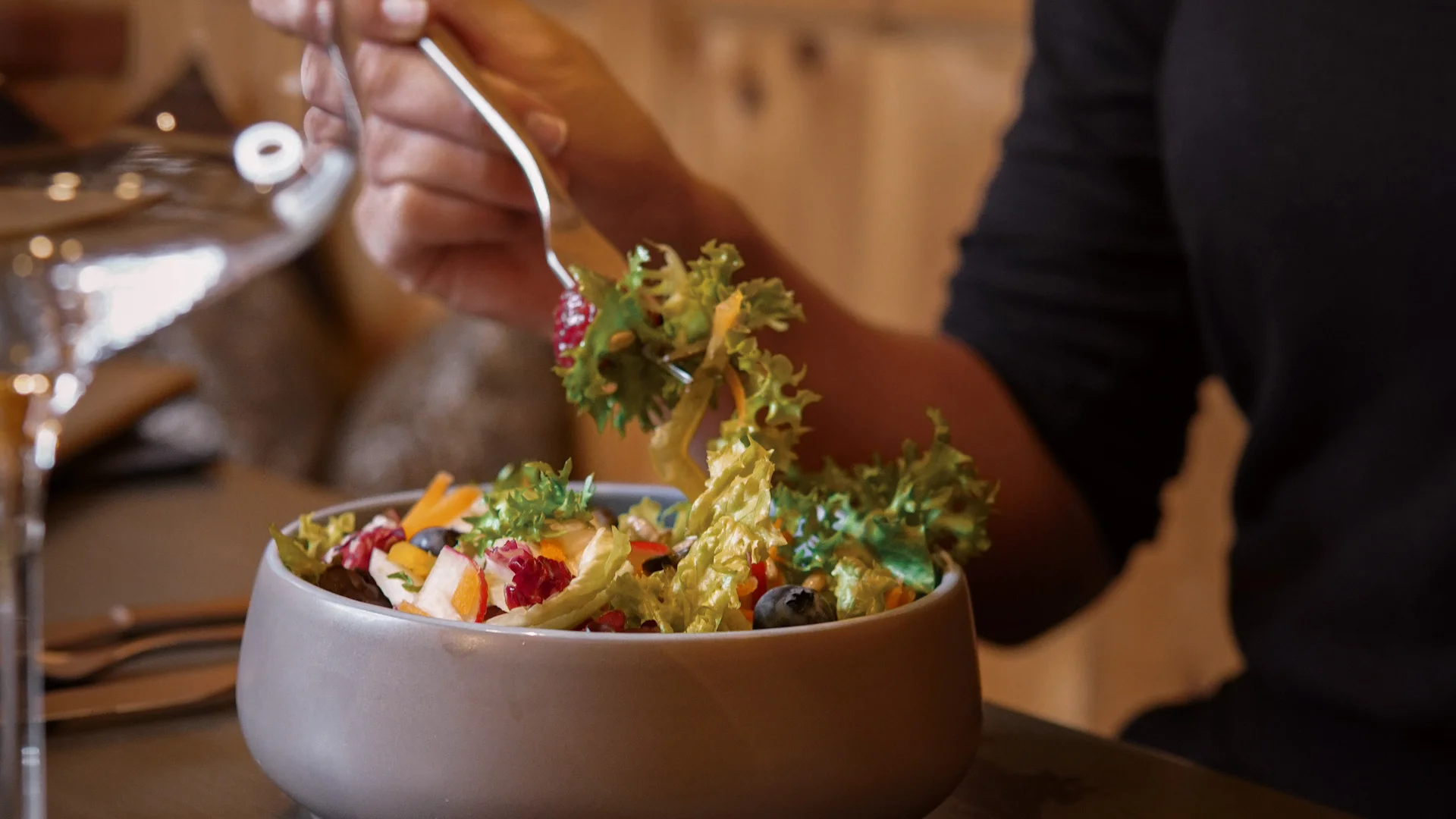 Person isst frischen gemischten Salat mit Gabel an einem Esstisch